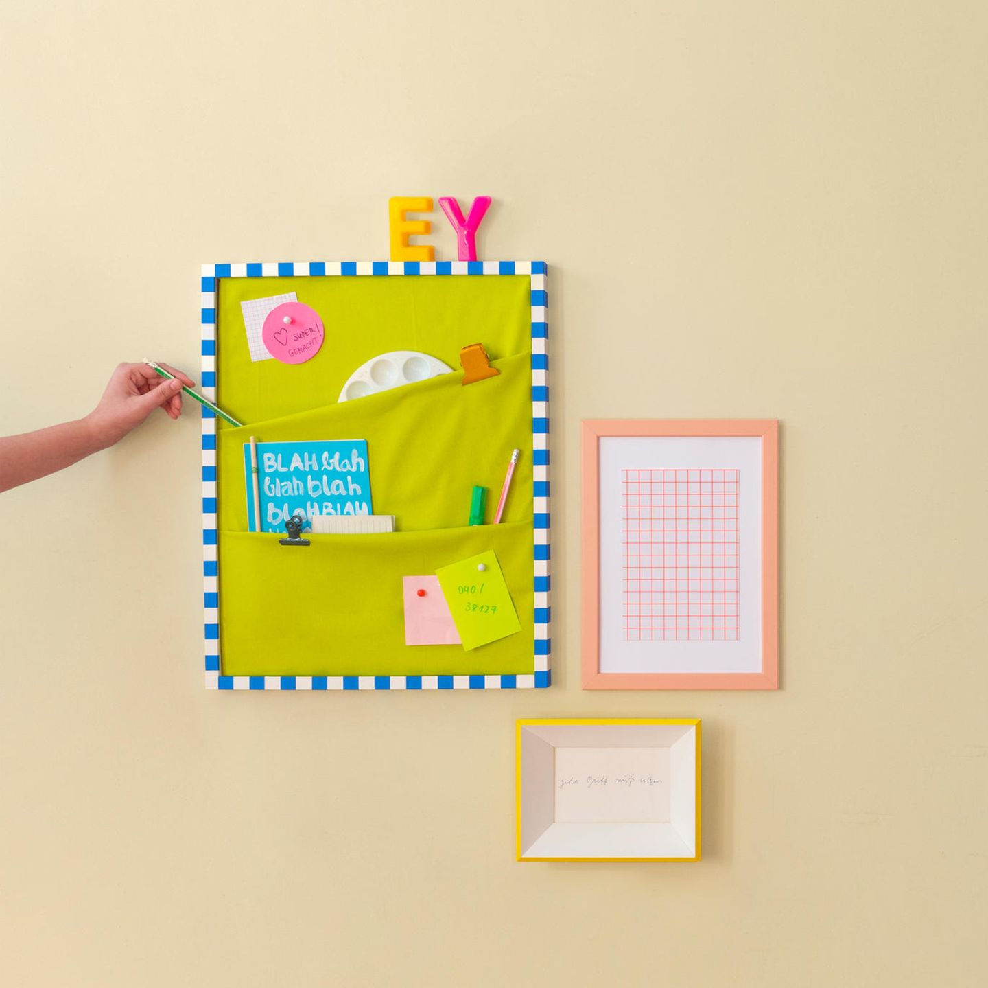 Pinnwand selber machen – An einer Wand hängt eine Pinnwand mit Taschen, darin sind unter anderem Stifte und eine Mischpalette