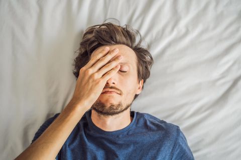 Ein Mann liegt im Bett und fasst sich an den Kopf