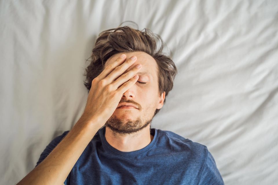 Ein Mann liegt im Bett und fasst sich an den Kopf