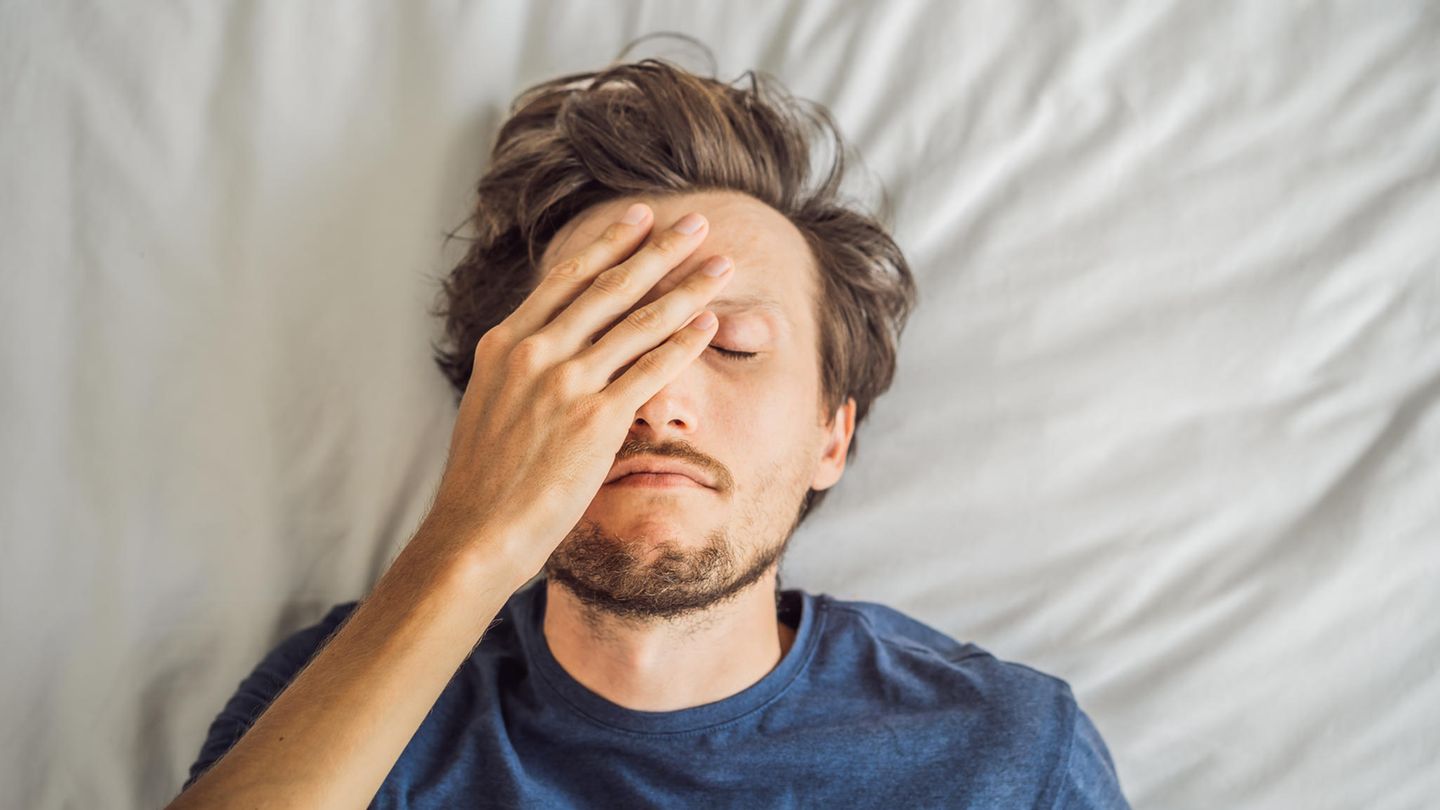 Ein Mann liegt im Bett und fasst sich an den Kopf