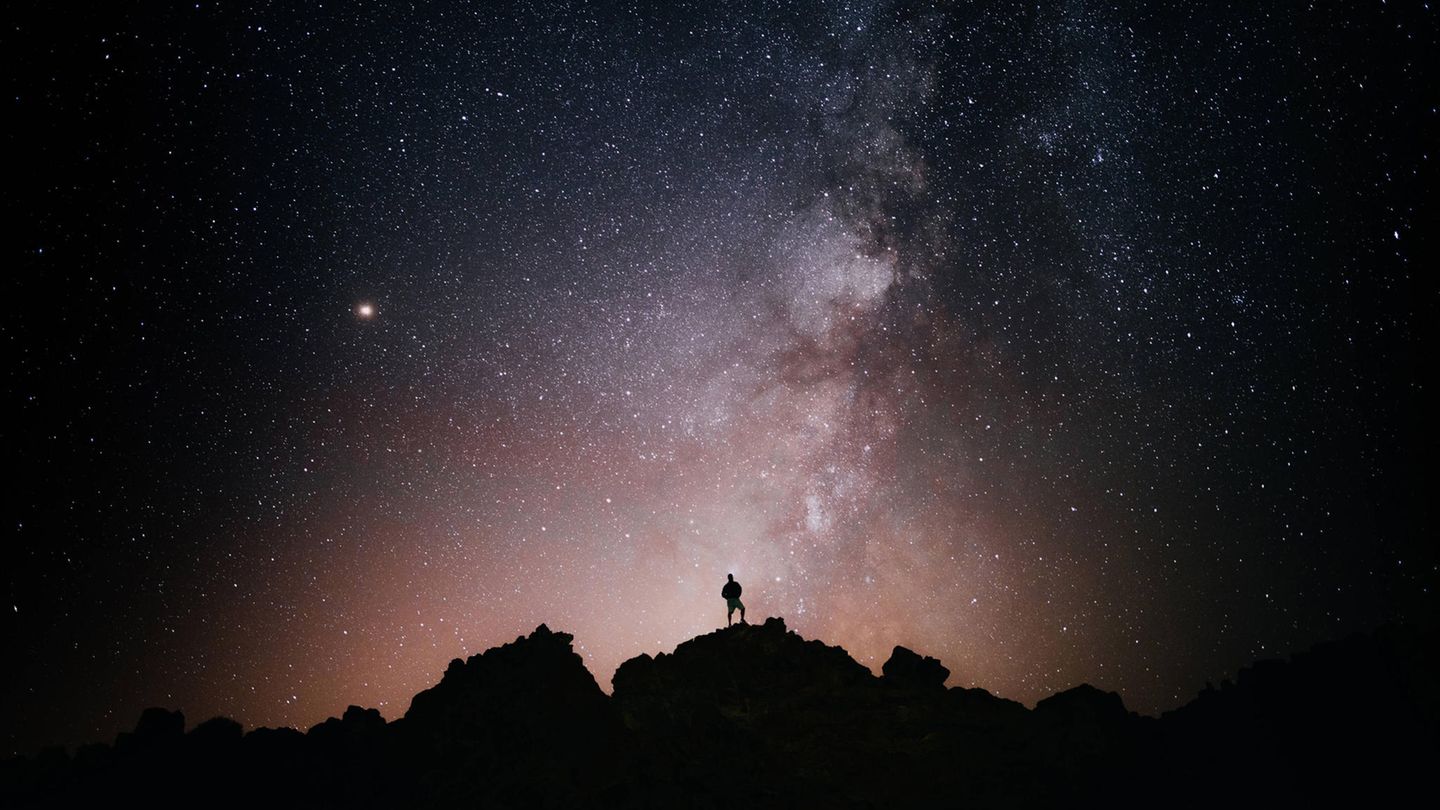 Ein Mann steht auf einem Berg und schaut in den Sternenhimmel