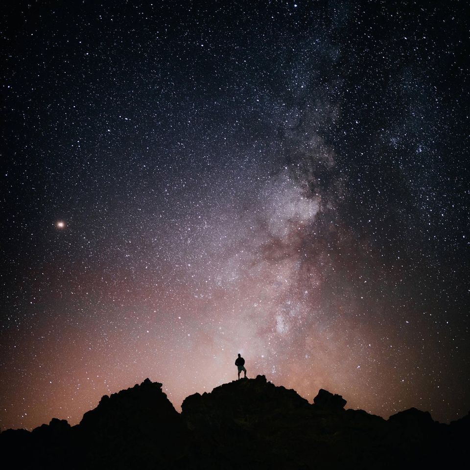 Ein Mann steht auf einem Berg und schaut in den Sternenhimmel