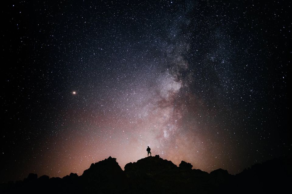 Ein Mann steht auf einem Berg und schaut in den Sternenhimmel