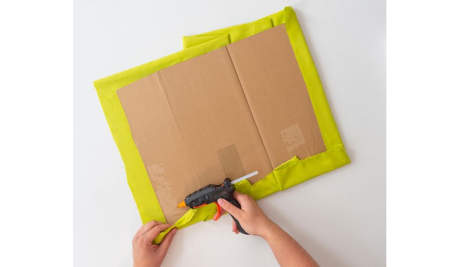 Pinnwand selber machen - grüner Baumwollstoff wird mit Heißkleber an einem Stück Pappe befestigt