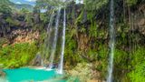 Wasserfall mit vielen grünen Pflanzen und blauem Wasser