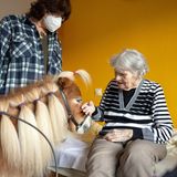 Ein Pony mit vielen Zöpfen steht vor dem Bett einer Heimbewohnerin und lässt sich streicheln