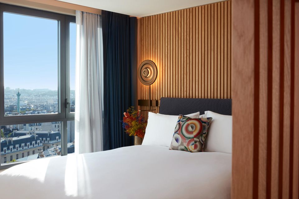 Blick auf das Bett in einem Hotelzimmer, dahinter die Skyline von Paris