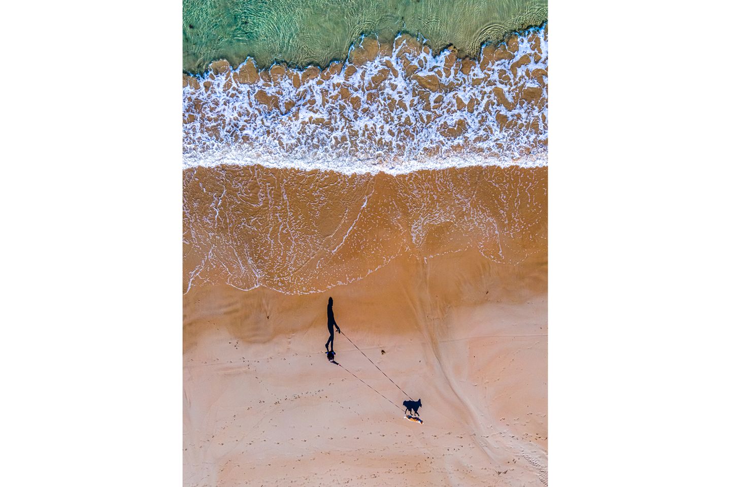 Dritter Platz der Kategorie "Dogs & People" 3rd Place - Russell Charters - Australia Walking the dog along the beach. Photo taken by DJI Mavic Air2 drone of my partner walking our dog, Luna. ( Focal length 24mm, F/2.8, 1/100 sec, ISO1000.)