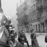 Feuerwehrmänner und SS-Truppen beobachten brennende Häsuer