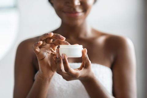 Eine Frau nimmt mit dem Finger etwas Body Butter aus einem weißen Tiegel auf.
