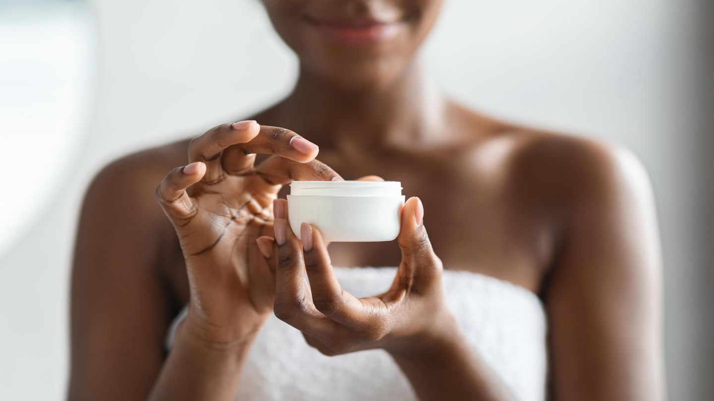 Eine Frau nimmt mit dem Finger etwas Body Butter aus einem weißen Tiegel auf.