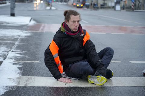 Ein Klimaaktivist der letzten Generation sitzt auf der Straße und schaut traurig
