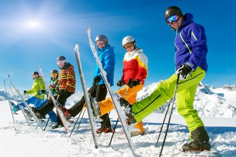 Packliste Skiurlaub: Eine Skigruppe in voller Montur und auf Skiern hat sich in einer Reihe aufgestellt.