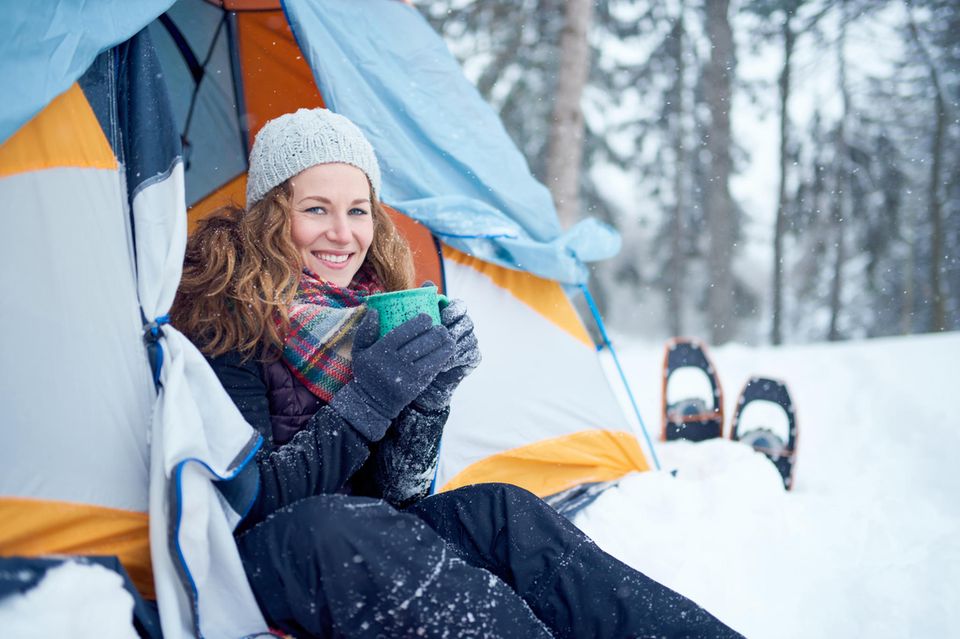 eine Frau sitzt im Zelteingang umgeben von Schnee