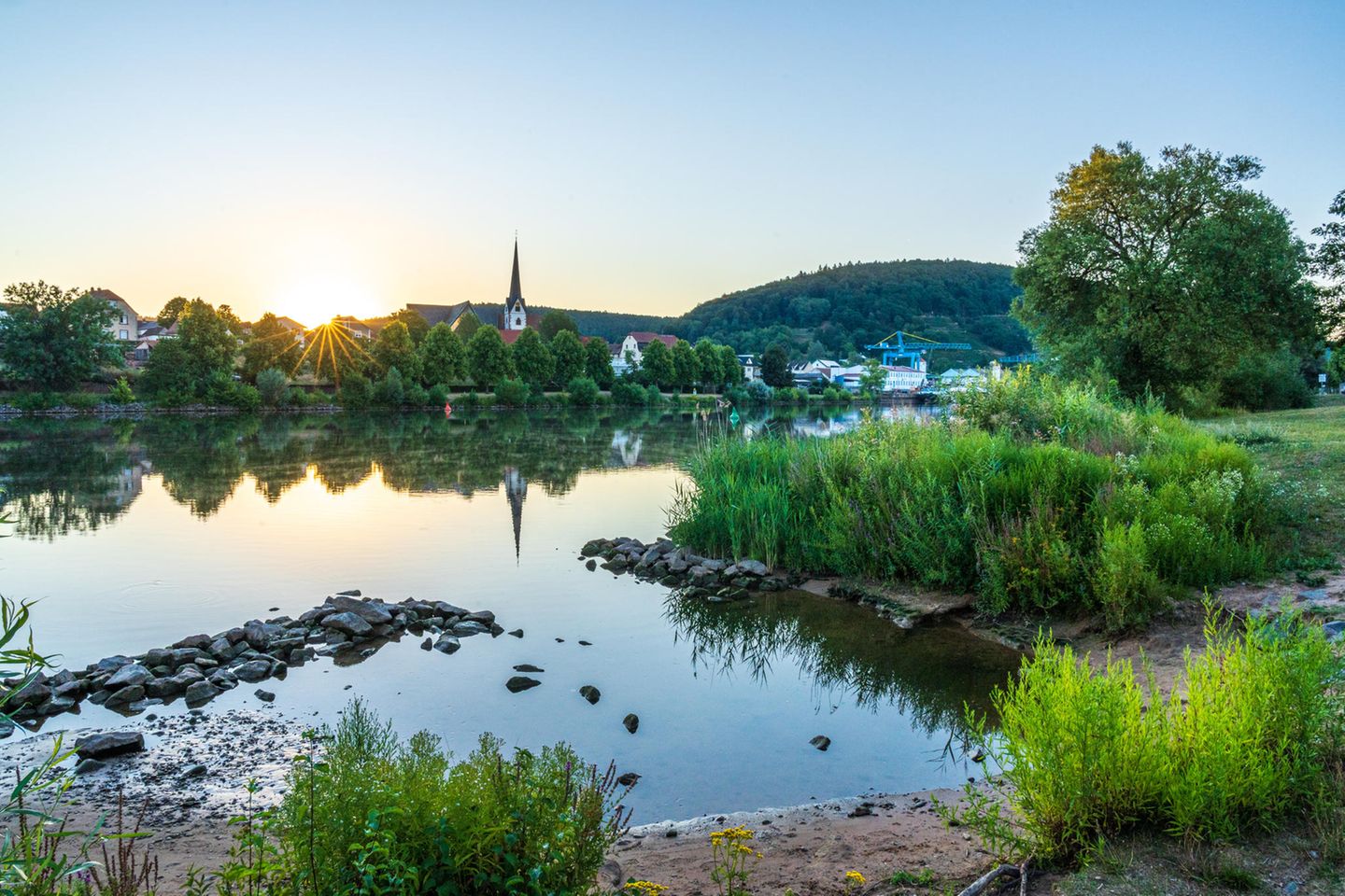 Gute Gründe fürs Frühaufstehen Blick über einen kleinen See auf einen Ort mit Kirchturm
