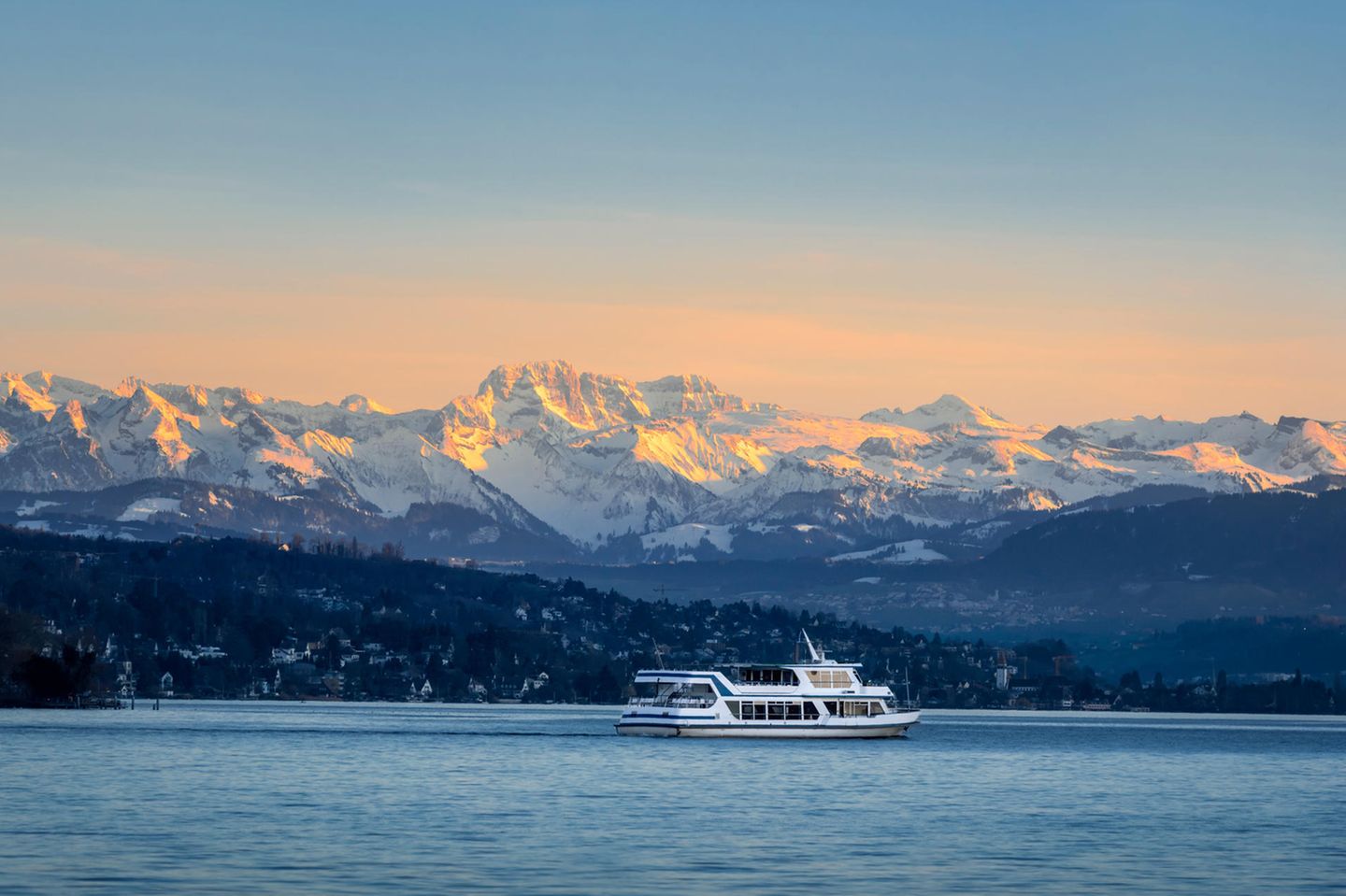 Zürich von der Seeseite bestaunen Kleines Schiff auf dem Zürichsee, im Hintergrund sind die Alpen zu sehen