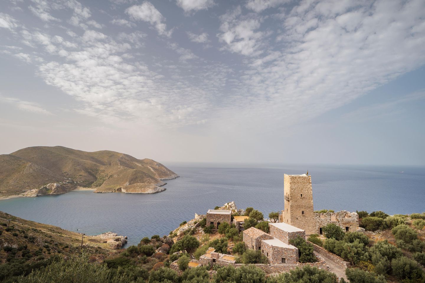 Tainaron Blue Retreat - Vathia, Griechenland Es ist wie ein Blick in die Ewigkeit: Bis zum Horizont ziehen die Wolken über das weite Blau des Mittelmeers. Die Blätter der knorrigen Olivenbäume sirren leise im Wind, mal rufen Möwen. Und hinter der Kante des Infinitypools treibt das Auge über nichts als Inseln, Felsen, Wasser, Himmel. Die Aussicht vom alten Wehrturm an der Südspitze der griechischen Halbinsel Mani auf dem Peloponnes ist ein Spektakel der Stille. Intensiv und atemraubend. Es gibt keine Nachbarn, kein Töpfeklappern, kein Kindergeschrei. Weder hupende Autos, noch plärrende Gettoblaster. Nur dieses kleine, intime Hotel Tainaron Blue Retreat mit seinen vier Zimmern auf felsigem Grund. Die Architekten und Gastgeber Kostas Zouvelos und Kassiani Theodorakakou haben den denkmalgeschützten Turm des Forts aus dem 19. Jahrhundert zu einer Oase mit besonderem Flair gemacht: Balken und Deckengewölbe wurden freigelegt, moderne Duschen, Waschbecken und Schreibtische schmiegen sich an den alten Stein. Draußen liegen wir auf Outdoor-Betten, über denen weiße Stoffe flattern. Zum Frühstück gibt es Granatäpfel vom eigenen Feld, frisch gebratenes Omelett, Kuchen und Joghurt aus der Region, am Abend ein mehrgängiges, saisonales Menü. Es duftet nach Pinien, Meer und Sommerwärme. Erst wenn die Sonne still im Meer versunken ist, gehen wir wieder rein, und wollen weniger von hier weg als je zuvor.