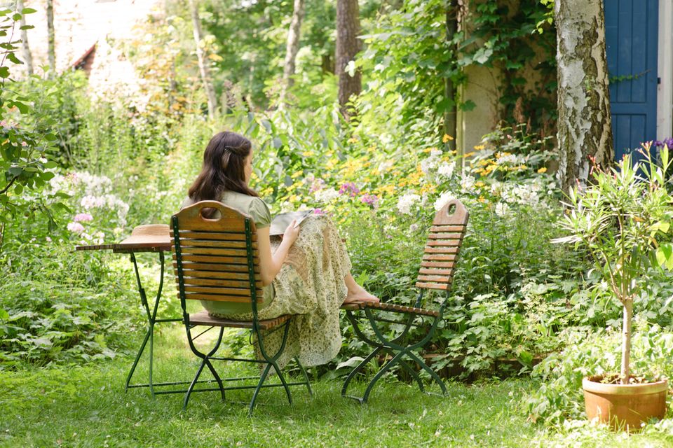 Frau sitzt im geschützten Garten