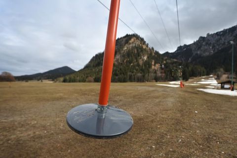 Hier läuft nichts: Teller eines Schleppliftes baumeln an einer Skipiste im bayerischen Schwangau, auf der noch Reste von Kunstschnee zu sehen sind