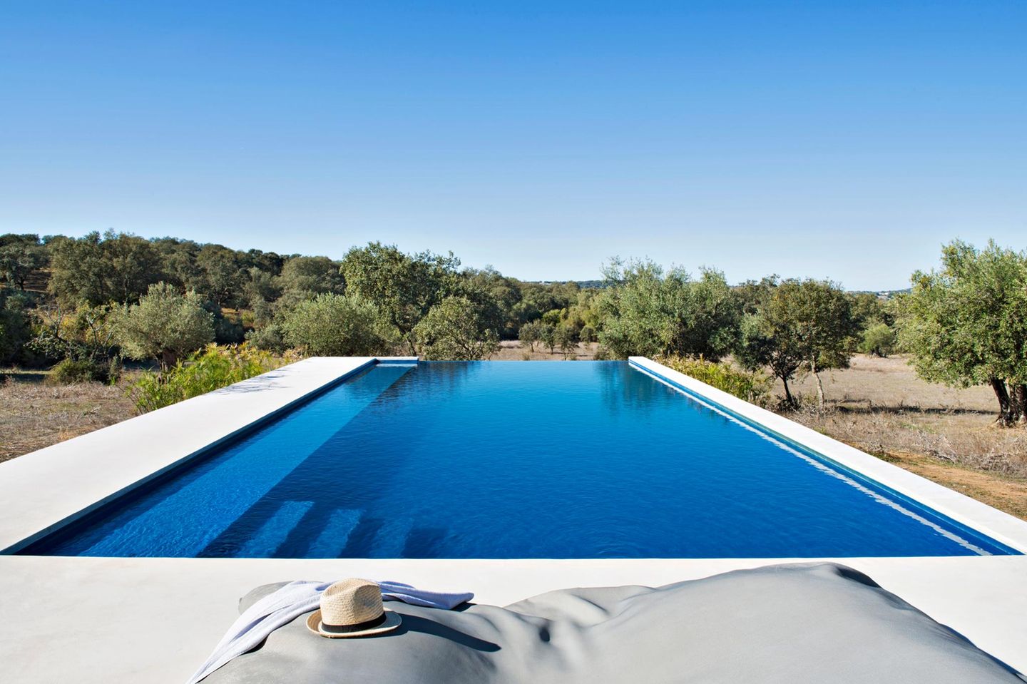 Villa Extramuros - Alentejo, Portugal Aus der Ferne wirkt er wie ein fehlgelandetes Ufo: ein grellweißer, brutalistischer Bau zwischen struppigen Eichen- und Olivenwäldern. Trotz aller Strenge ist die Villa Extramuros im Nirgendwo Südportugals ein irre gemütlicher Zufluchtsort. Städte sind fern. Es gibt nichts zu tun, außer in den fünf durchdesignten Zimmern auszuschlafen, ein paar Bahnen im Infinitypool zu ziehen oder stundenlang zu spazieren – bis der Kopf so herrlich leer ist wie die Landschaft.