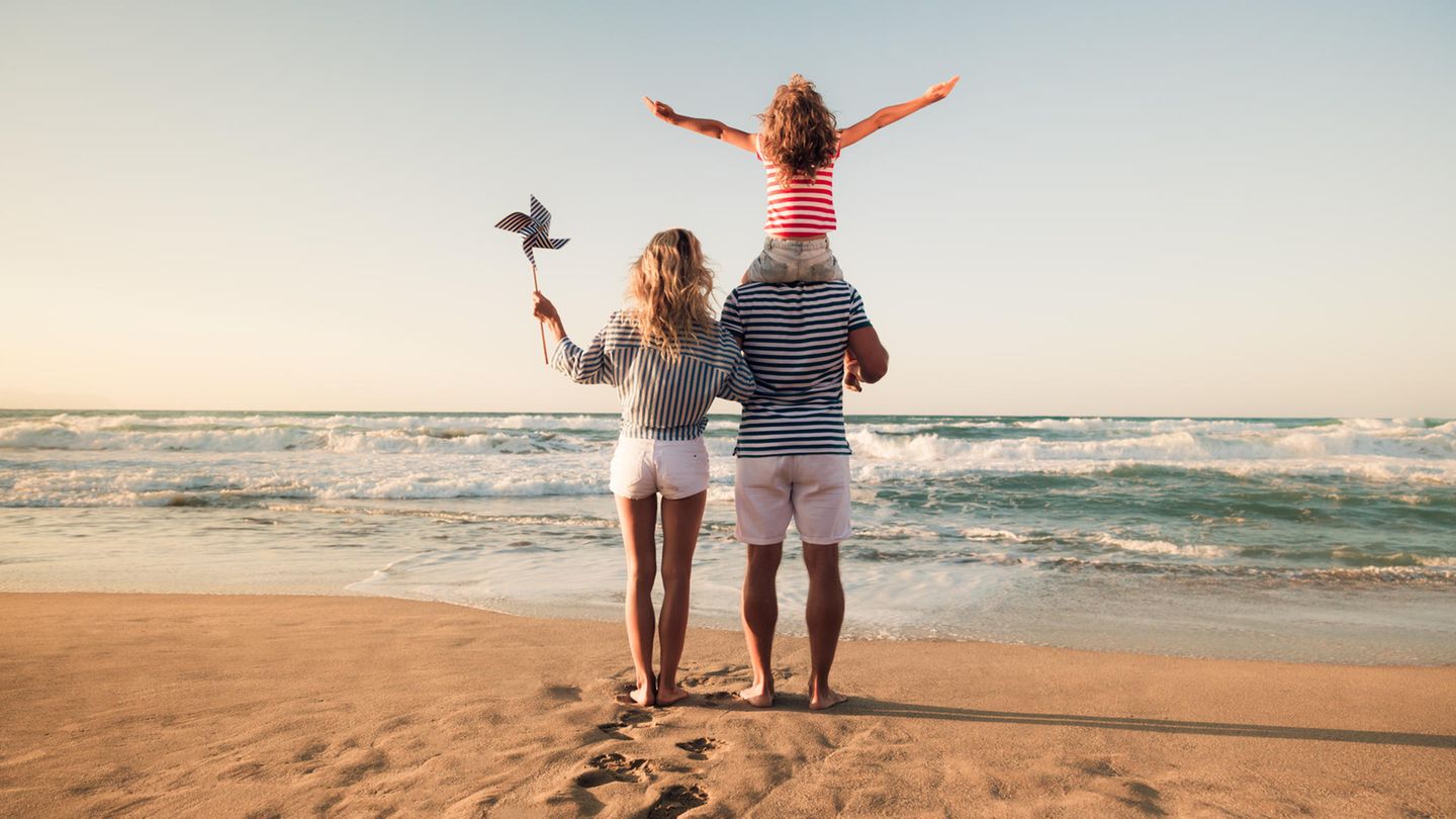 Familie steht am Strand und blickt aufs Meer