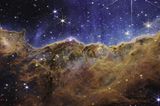 Wie eine Bergkette im letzten Abendlicht leuchtet der Carina-Nebel. Das fast dreidimensional wirkende Bild zeigt eine Region, die in der Astronomie »kosmische Kliffs« heißen. Im blauen Hintergrund schweben Tausende junge, sehr masse-reiche Sterne. Die starke UV-Strahlung und die Sonnenwinde, die von ihnen ausgehen, formen im Rand der braunen Staub- und Gaswolke bizarre Strukturen, die sich teils über mehrere Lichtjahre erstrecken