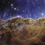 Wie eine Bergkette im letzten Abendlicht leuchtet der Carina-Nebel. Das fast dreidimensional wirkende Bild zeigt eine Region, die in der Astronomie »kosmische Kliffs« heißen. Im blauen Hintergrund schweben Tausende junge, sehr masse-reiche Sterne. Die starke UV-Strahlung und die Sonnenwinde, die von ihnen ausgehen, formen im Rand der braunen Staub- und Gaswolke bizarre Strukturen, die sich teils über mehrere Lichtjahre erstrecken