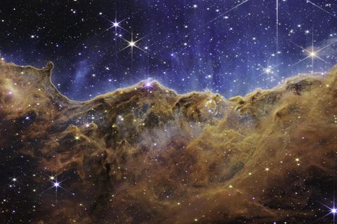 Wie eine Bergkette im letzten Abendlicht leuchtet der Carina-Nebel. Das fast dreidimensional wirkende Bild zeigt eine Region, die in der Astronomie »kosmische Kliffs« heißen. Im blauen Hintergrund schweben Tausende junge, sehr masse-reiche Sterne. Die starke UV-Strahlung und die Sonnenwinde, die von ihnen ausgehen, formen im Rand der braunen Staub- und Gaswolke bizarre Strukturen, die sich teils über mehrere Lichtjahre erstrecken