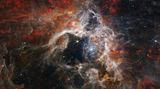 Im Tarantula-Nebel, der 161 000 Lichtjahre von der Erde entfernt ist, befindet sich die größte und hellste Sternbildungsregion in unserer näheren kosmischen Umgebung. Im Herz des Nebels leuchten strahlend blau dargestellt unzählige junge, sehr heiße Sonnen. Ihre massive Strahlung hat Gas und Staub um sie herum hinweggeblasen und so eine Art Höhle geformt