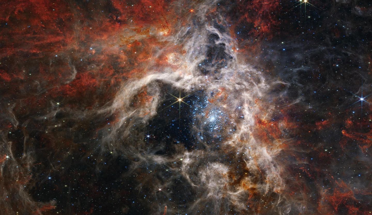 Im Tarantula-Nebel, der 161 000 Lichtjahre von der Erde entfernt ist, befindet sich die größte und hellste Sternbildungsregion in unserer näheren kosmischen Umgebung. Im Herz des Nebels leuchten strahlend blau dargestellt unzählige junge, sehr heiße Sonnen. Ihre massive Strahlung hat Gas und Staub um sie herum hinweggeblasen und so eine Art Höhle geformt