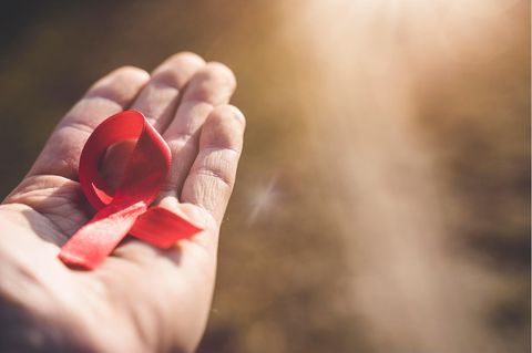 Hand hält eine rote Schleife gegen die Sonne. Symbolbild zum Thema Aids