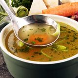 Eine Suppenkelle in einer großen Schüssel Gemüsebrühe