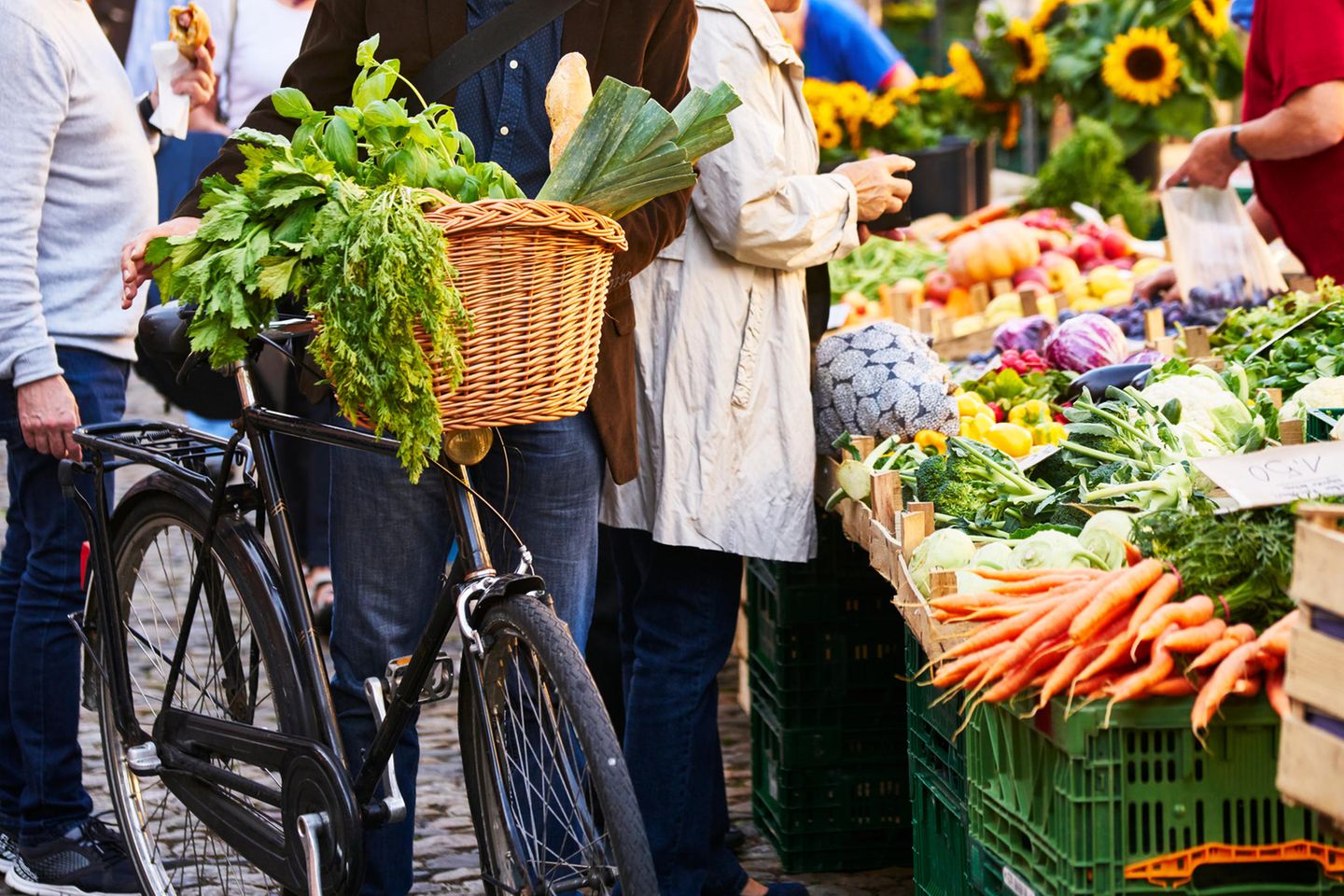 Menschen stehen vor einem Gemüsestand auf dem Wochenmarkt