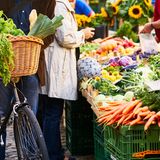Menschen stehen vor einem Gemüsestand auf dem Wochenmarkt
