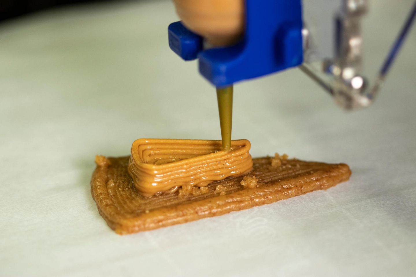 Ein 3D-Drucker spritzt eine braune Masse in Kuchenform Ein 3D-Drucker spritzt eine braune Masse in Kuchenform