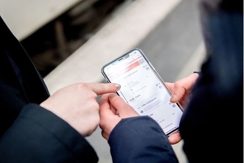 Hände mit Handy in der Hand, auf dem die DB Navigator-App geöffnet ist
