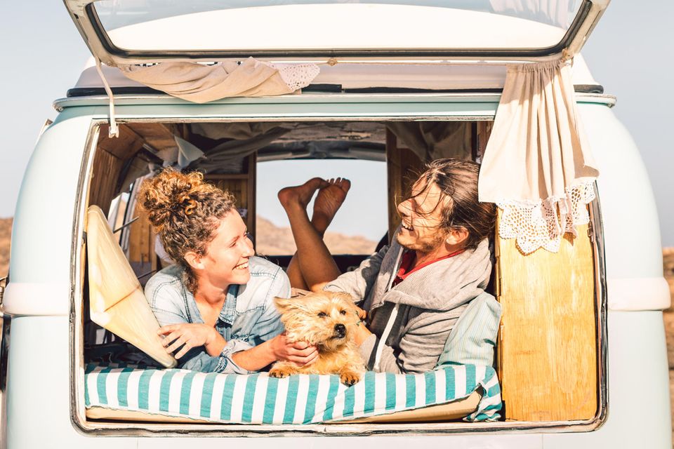 Eine lächelndes Pärchen mit Hund liegt entspannt im Campervan.