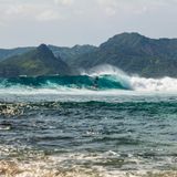 Surfer auf einer Welle, im Hintergrund sind Berge