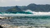 Surfer auf einer Welle, im Hintergrund sind Berge