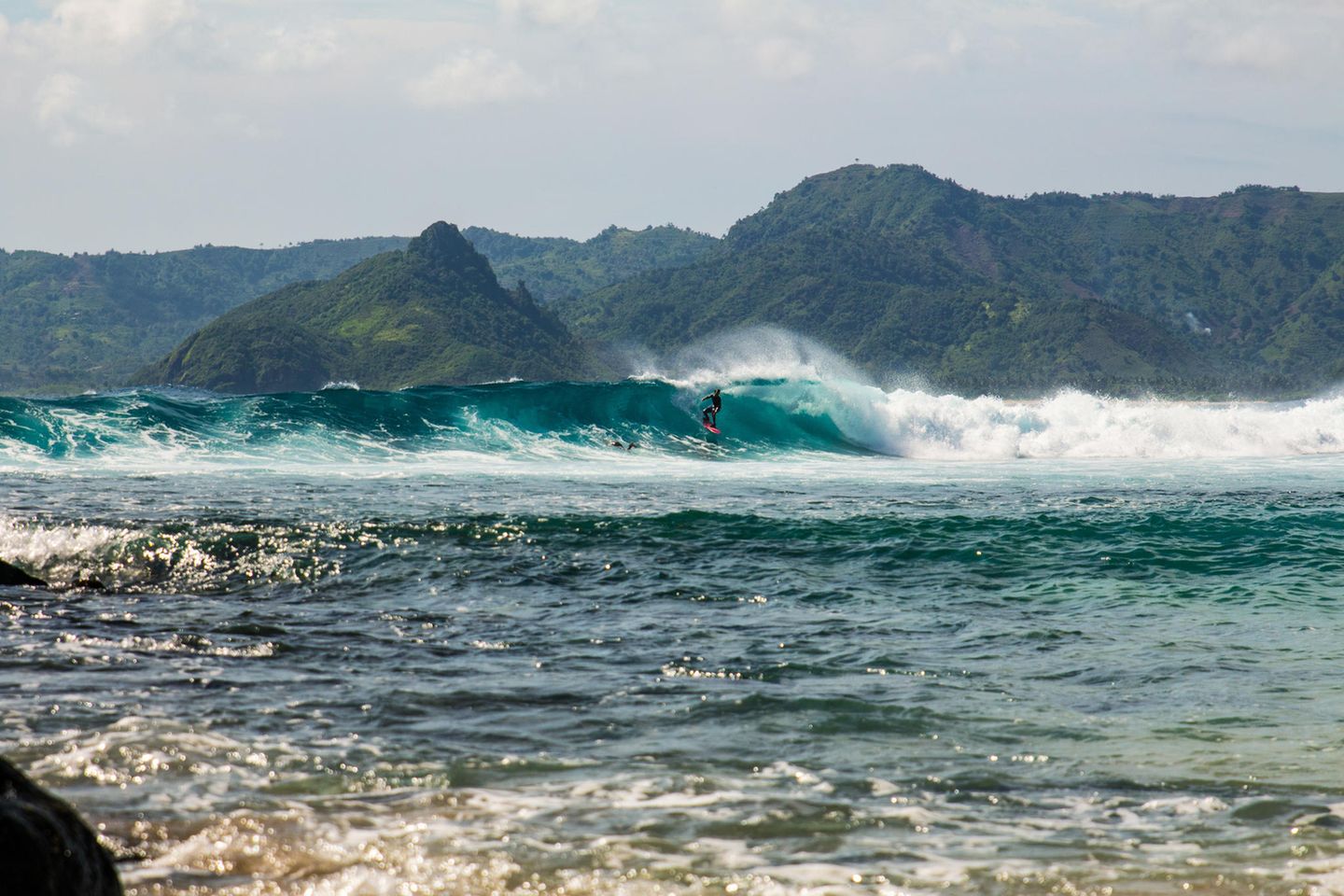 Lombok – die perfekte Welle Surfer auf einer Welle, im Hintergrund sind Berge