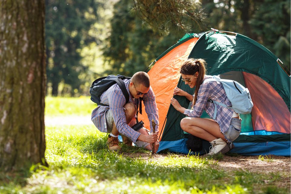 Ein junges Pärchen baut gemeinsam ein Zelt auf.