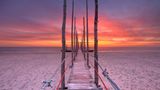 Schmaler Holzsteg am Strand bei Sonnenuntergang