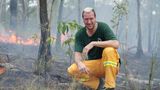 Pascal Hens kniet in einem Wald, hinter ihm ist Feuer zu sehen