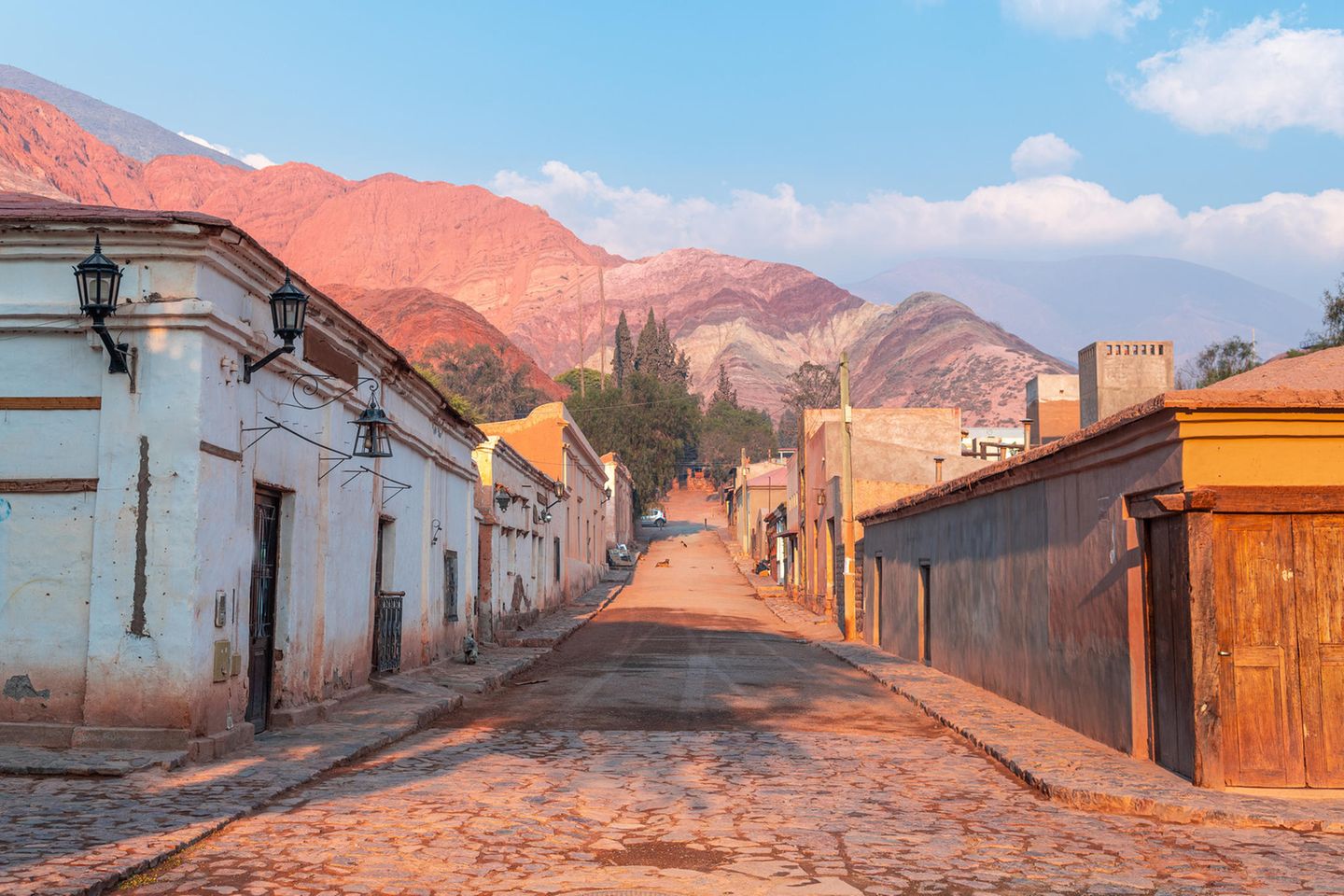 Quebrada de Humahuaca –Tuschkasten der Erdgeschichte Gepflasterte Straße mit kleinen Häusern an der Seite und einem Berg im Hintergrund, der verschieden farbige Schichten hat