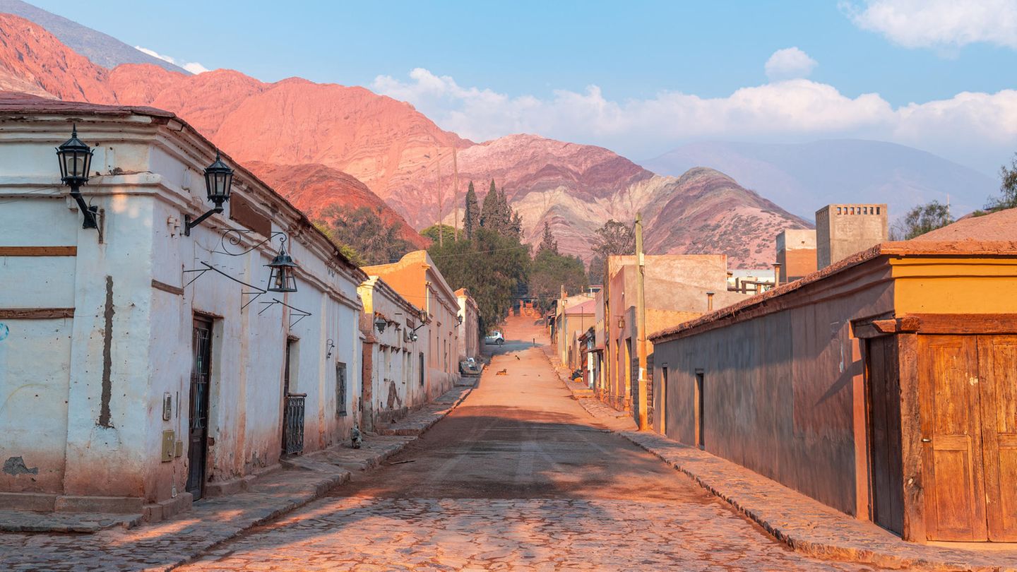 Quebrada de Humahuaca –Tuschkasten der Erdgeschichte Gepflasterte Straße mit kleinen Häusern an der Seite und einem Berg im Hintergrund, der verschieden farbige Schichten hat