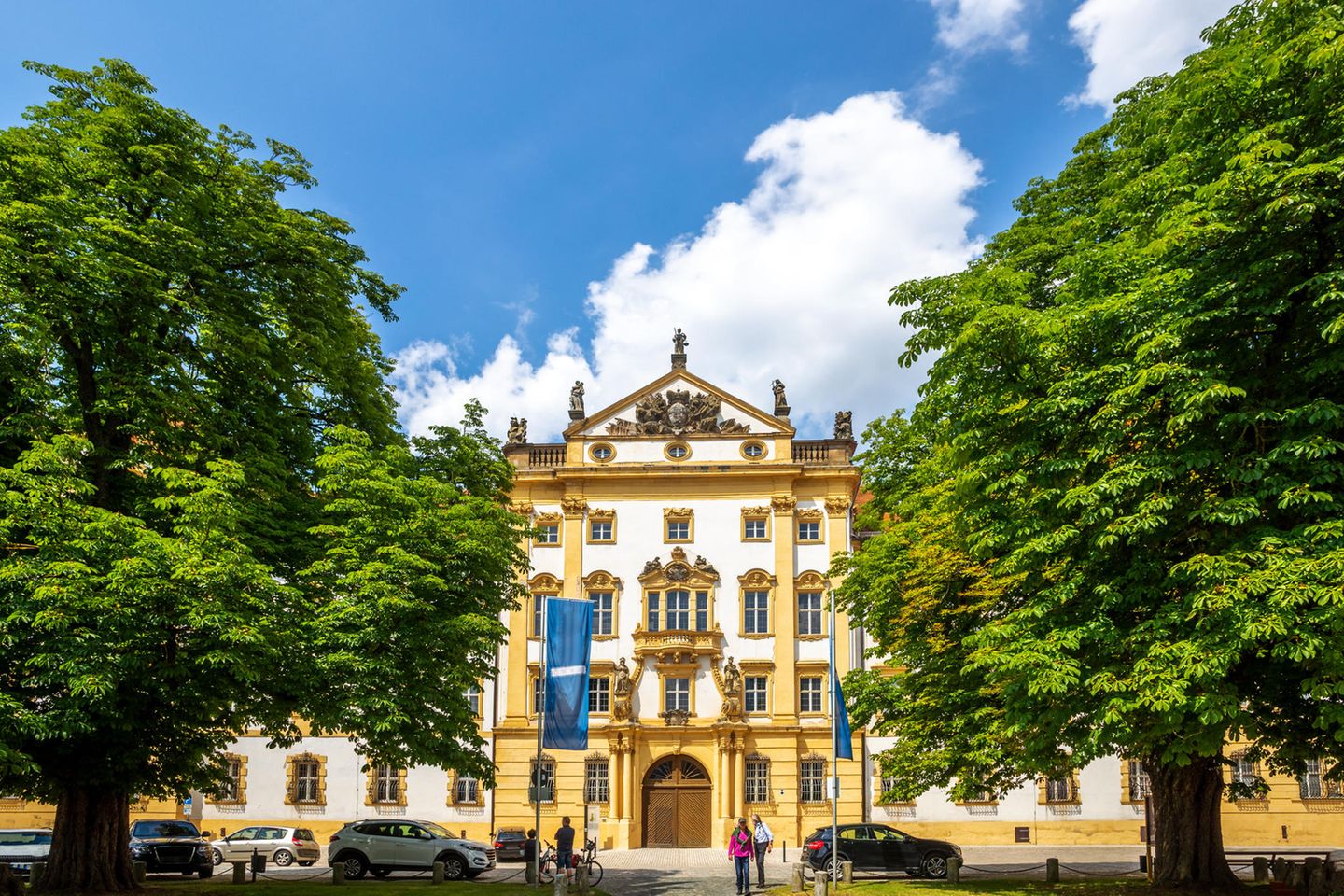 Ellingen – Perle des fränkischen Barocks Gelb-weißes Schloss mit grünen Bäumen davor bei Sonnenschein