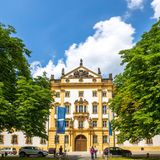 Gelb-weißes Schloss mit grünen Bäumen davor bei Sonnenschein