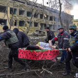 Eine schwangere Frau wird von mehreren Männern durch rauchende Trümmer getragen