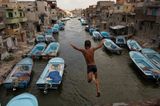 Ein Junge springt in einen Kanal, in dem viele blaue Boote liegen