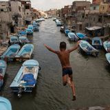 Ein Junge springt in einen Kanal, in dem viele blaue Boote liegen